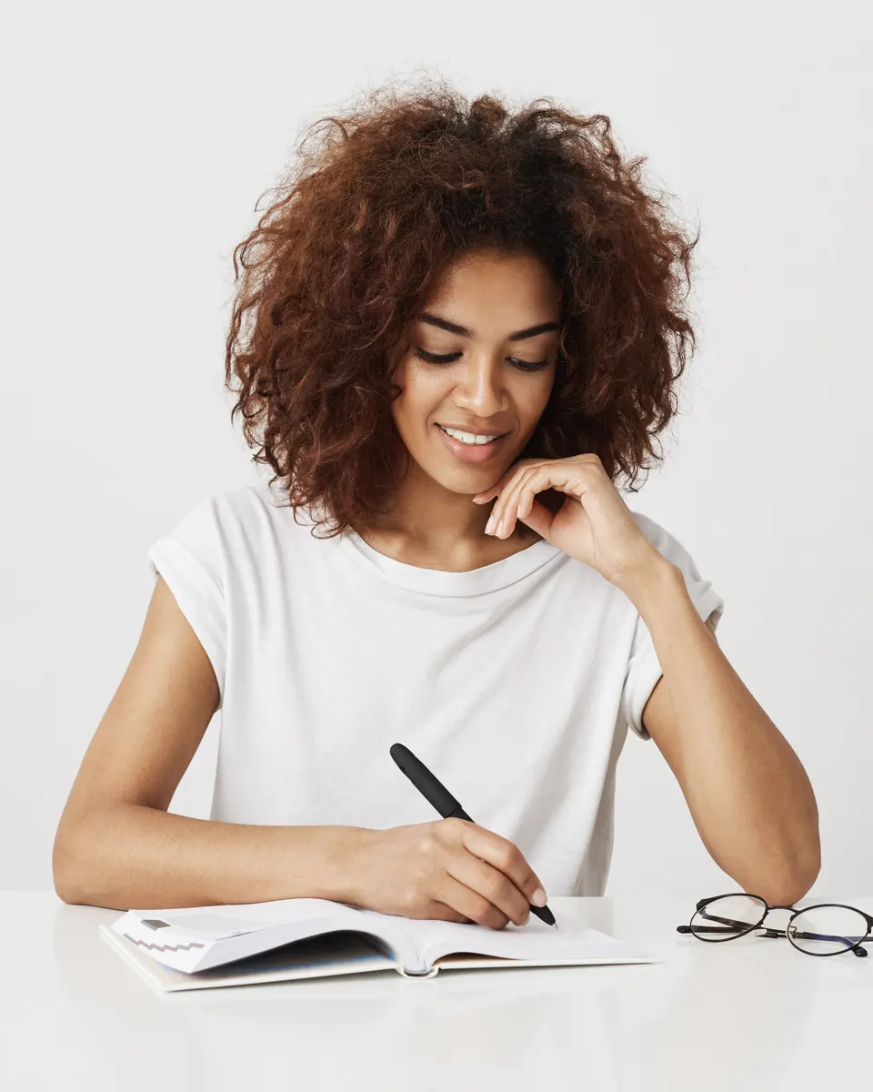 Una candidata sonriente prepara el examen cívico francés en su escritorio y toma notas en un cuaderno.